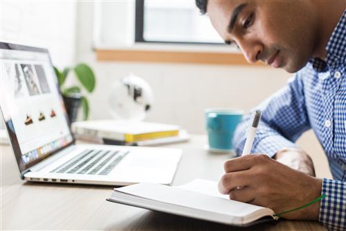 student writing in notebook, laptop 